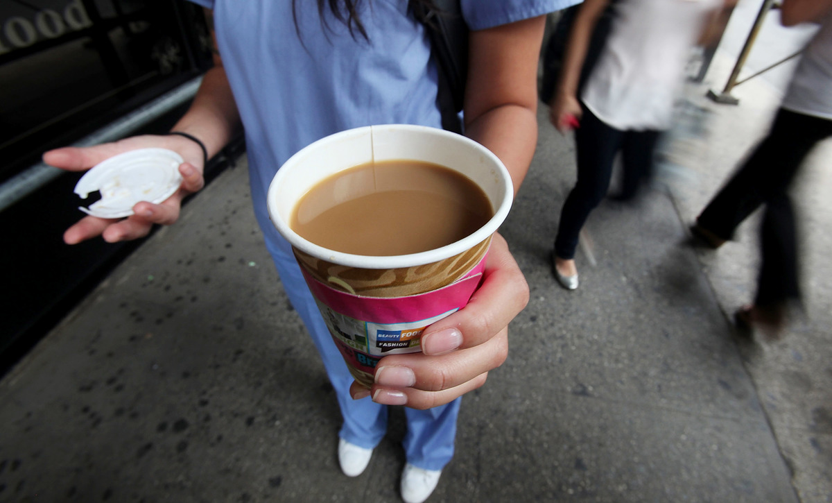 A woman holds a to-go cup of coffee on the street.