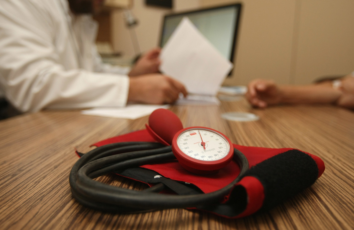 A doctor speaks to a patient as a sphygmomanometer, or blood pressure meter, lies on his desk.