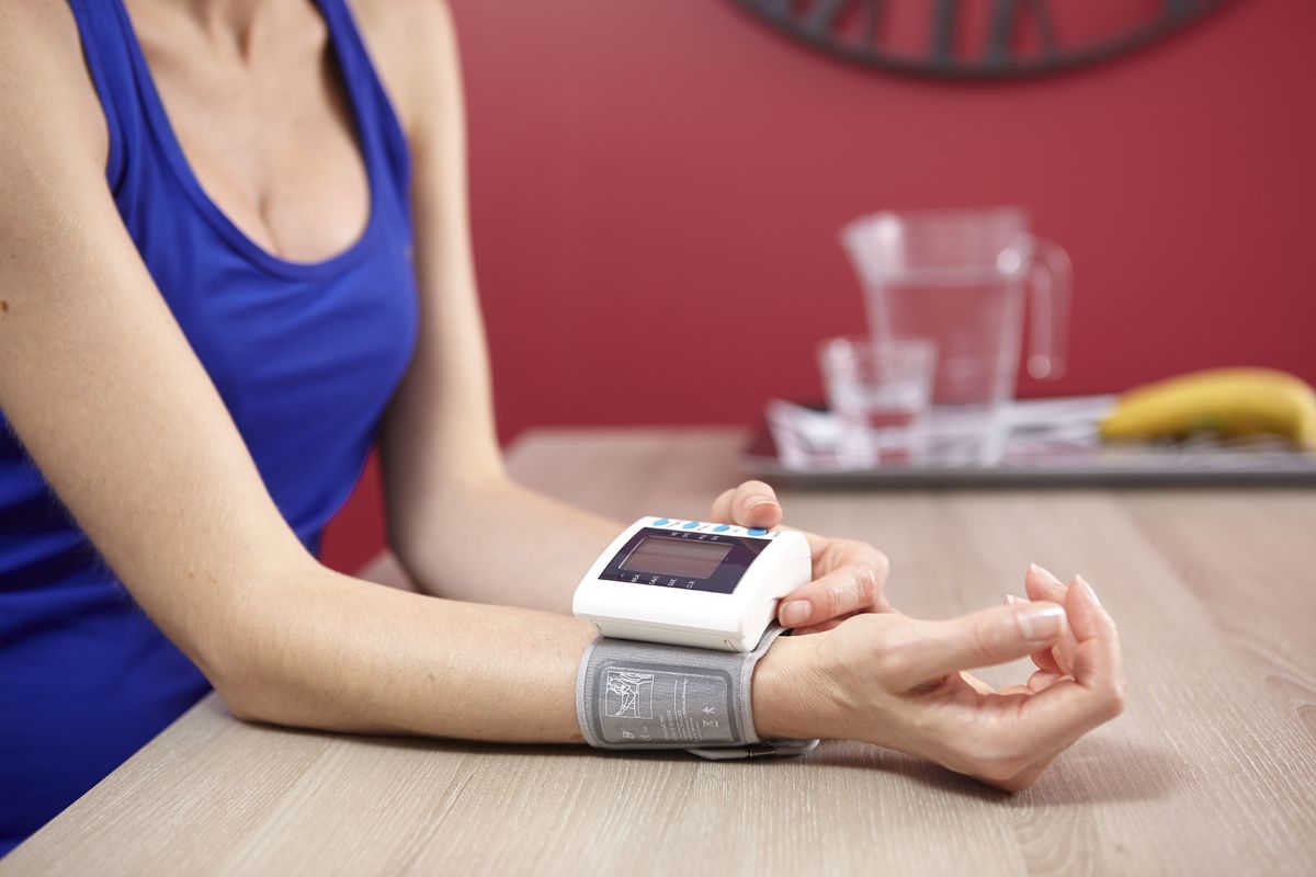 A woman measures her blood pressure at her kitchen table.